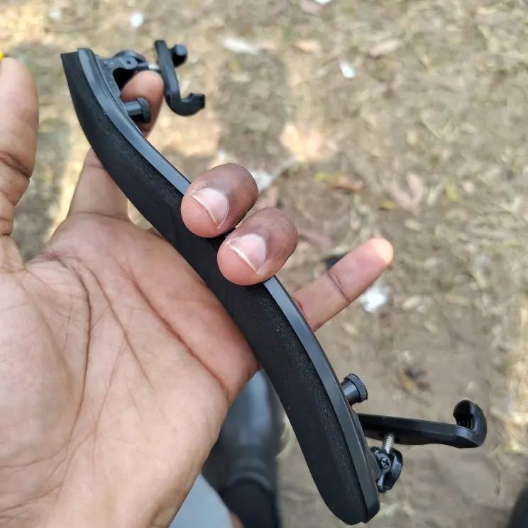 A hand holding the black shoulder rest outdoors, showing its foldable hook feet, photographed by Thomas B., a verified buyer